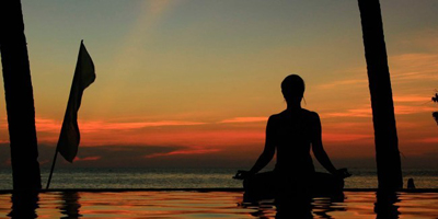 woman meditating on a sea beach under colorful enening sky